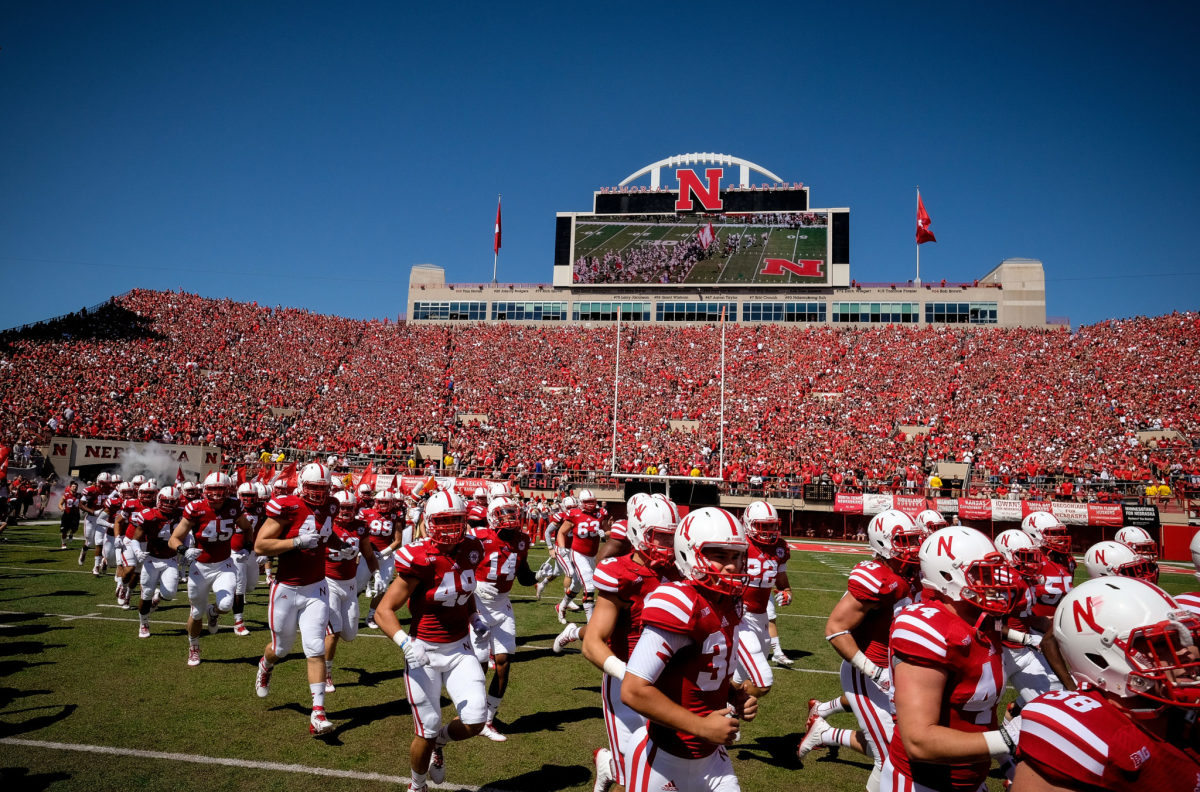 Nebraska football players, who compete in the Big Ten, run onto the field.