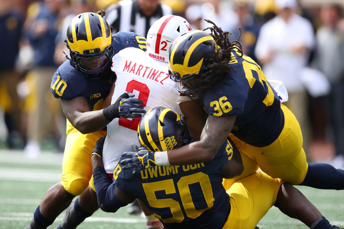 Michael Dwumfour, Devin Gil, and a Michigan teammate tackle an opponent.