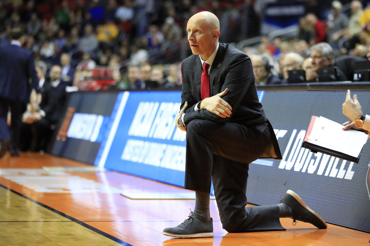 Louisville Cardinals head coach Chris Mack kneeling on the sideline during a game.
