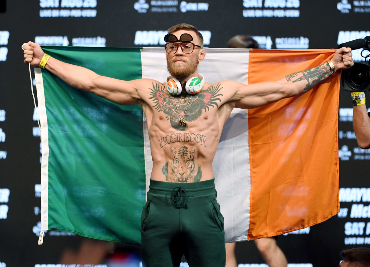 Conor McGregor wearing headphones and sunglasses while holding the Irish flag.