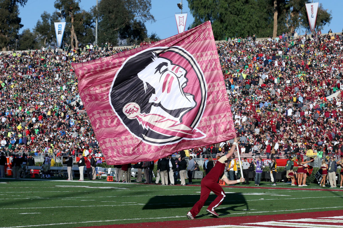 A Florida State cheerleader running around while holding a flag with the team's logo on it.