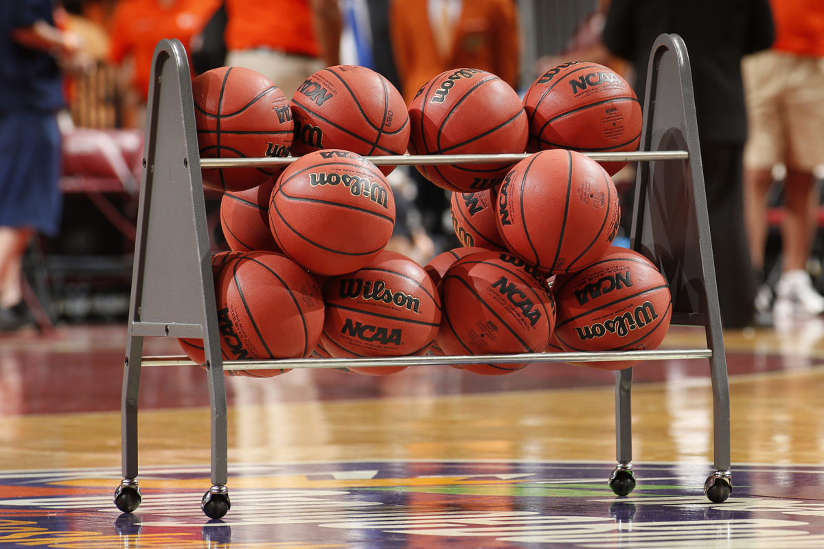 NCAA basketballs sitting in a ball rack on the court.