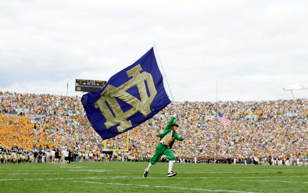 Notre Dame's mascot running with a flag on the football field.