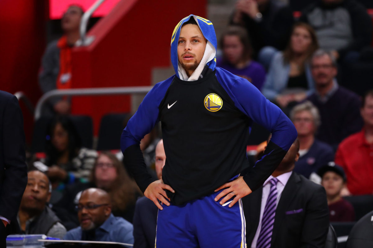 Golden State Warriors star Stephen Curry standing on the sideline with a towel wrapped around his head.