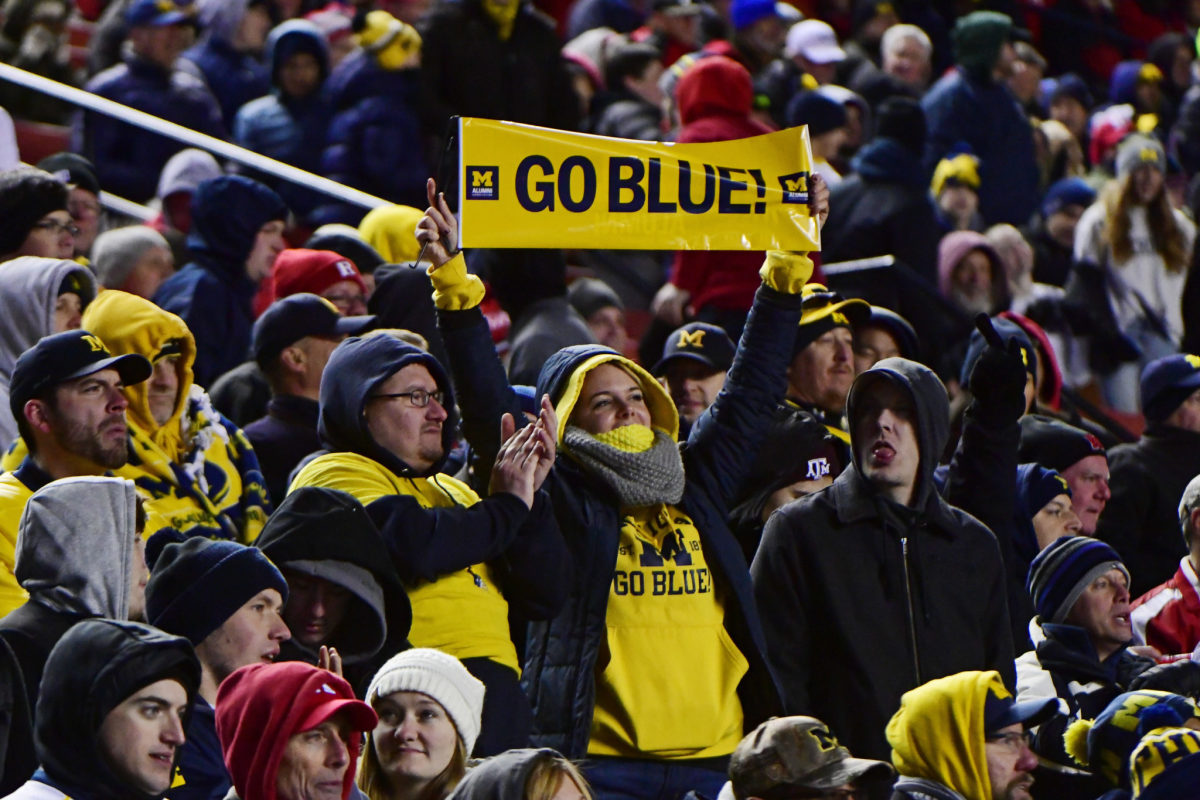 A Michigan fan holding up a sign that says "Go Blue" during a football game.
