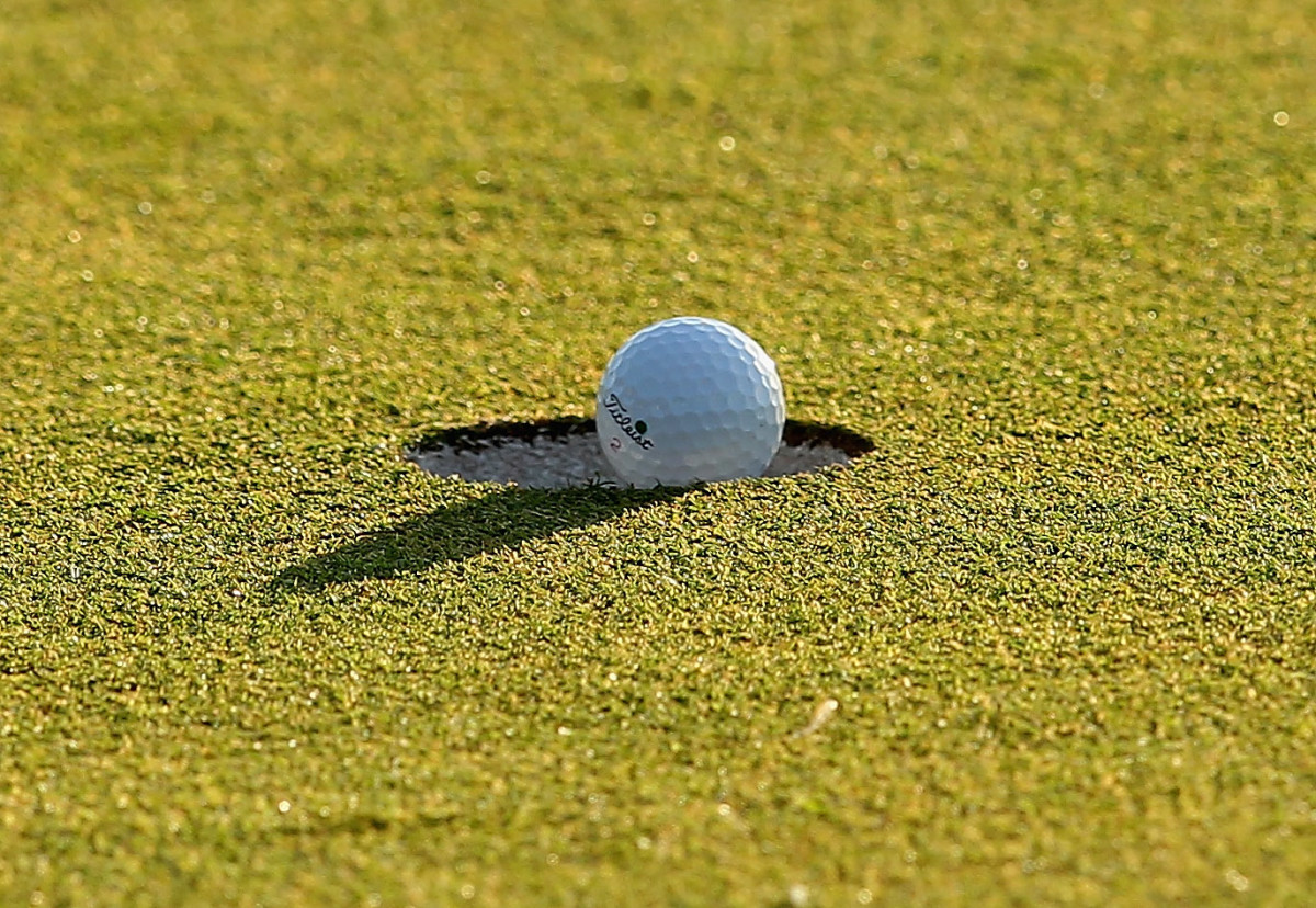 A golf ball falling into the cup.
