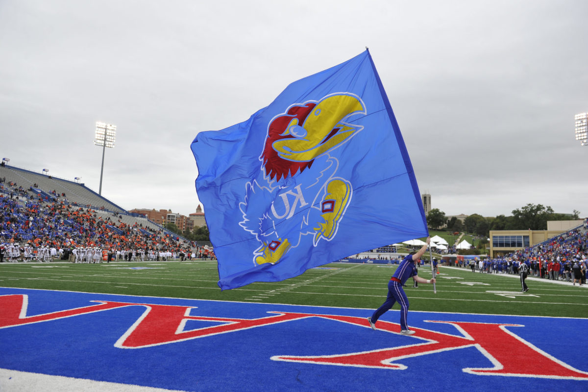 Kansas cheerleader runs with a Jayhawk flag during football game.