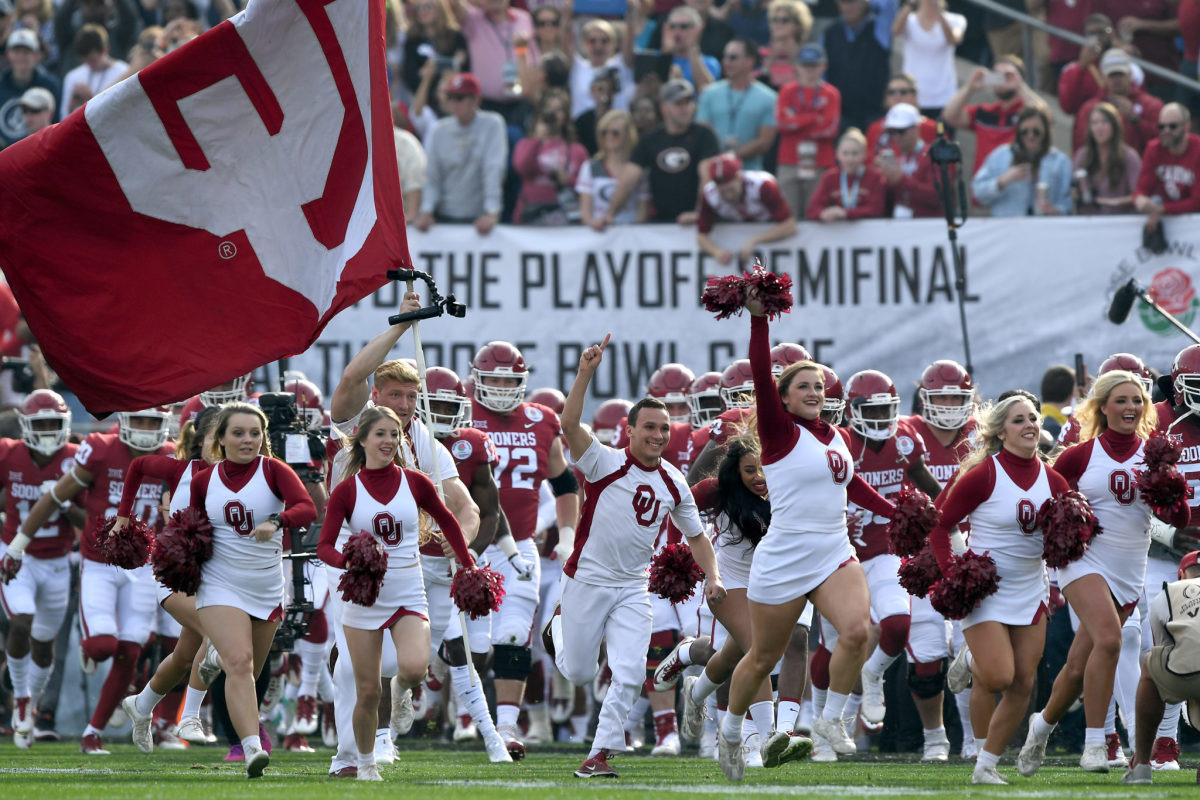 Oklahoma's cheerleaders leading the football team onto the field.