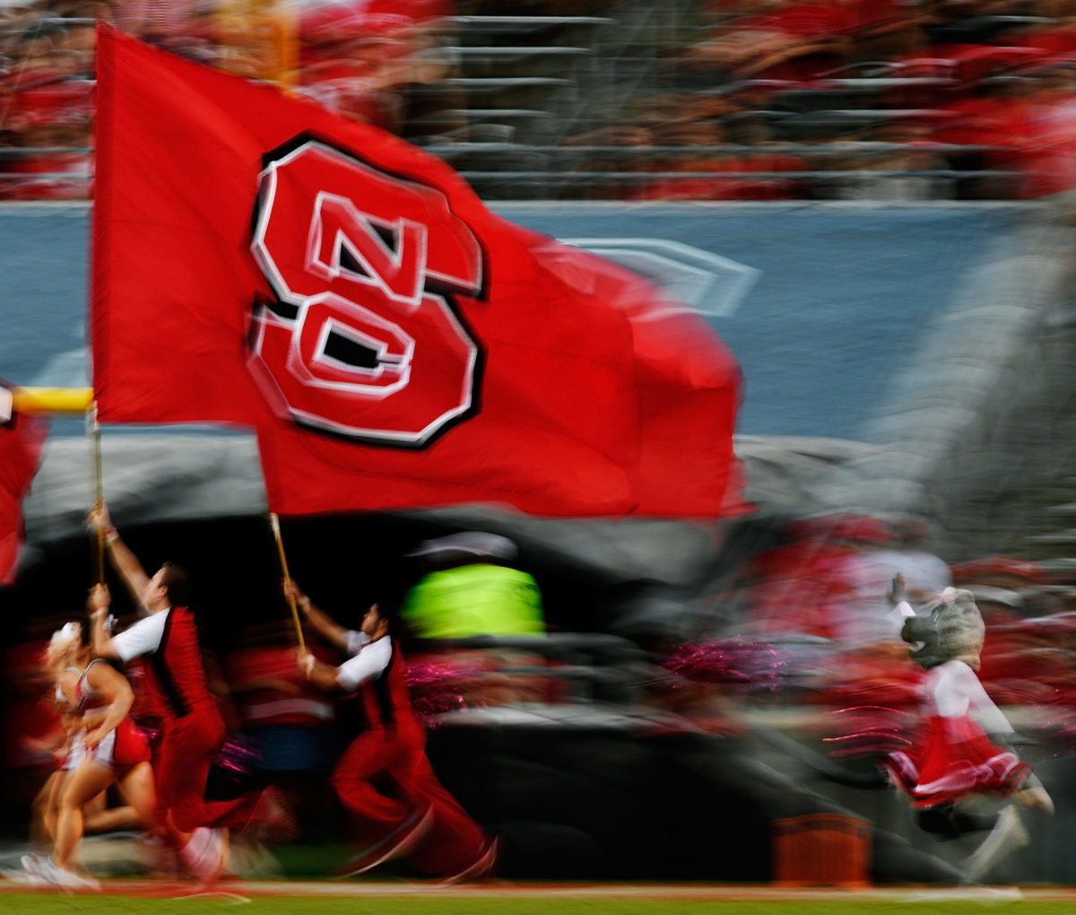 An NC State cheerleader running with a flag.