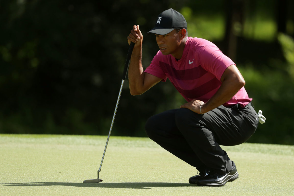 Tiger Woods crouching down on the putting green.