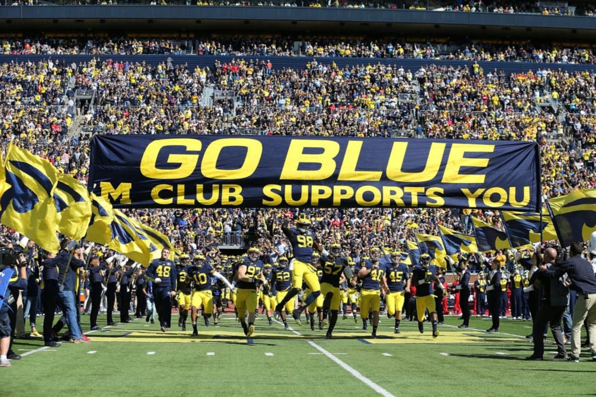 Michigan football players run under the "Go Blue" banner before a home game.