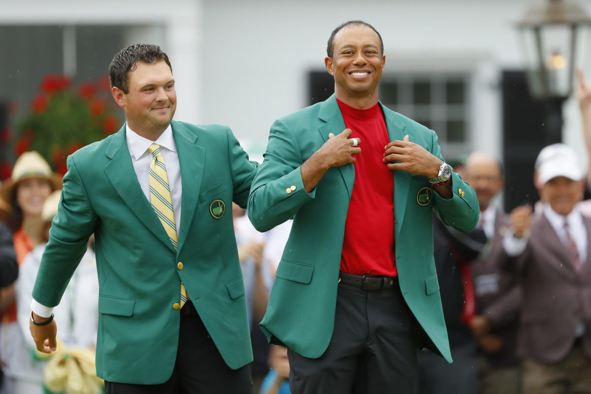 Tiger Woods putting on his green jacket as previous Masters winner Patrick Reed watches.