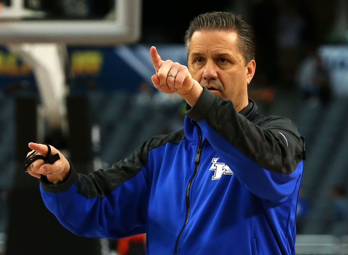 John Calipari wearing a Kentucky pullover while pointing with his left hand.