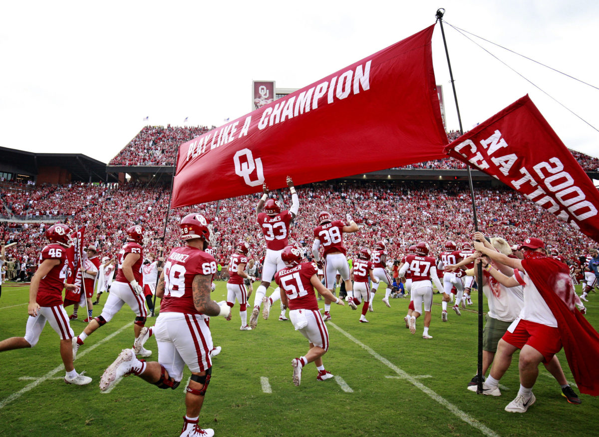 Oklahoma Sooners football players running onto the field before a game.