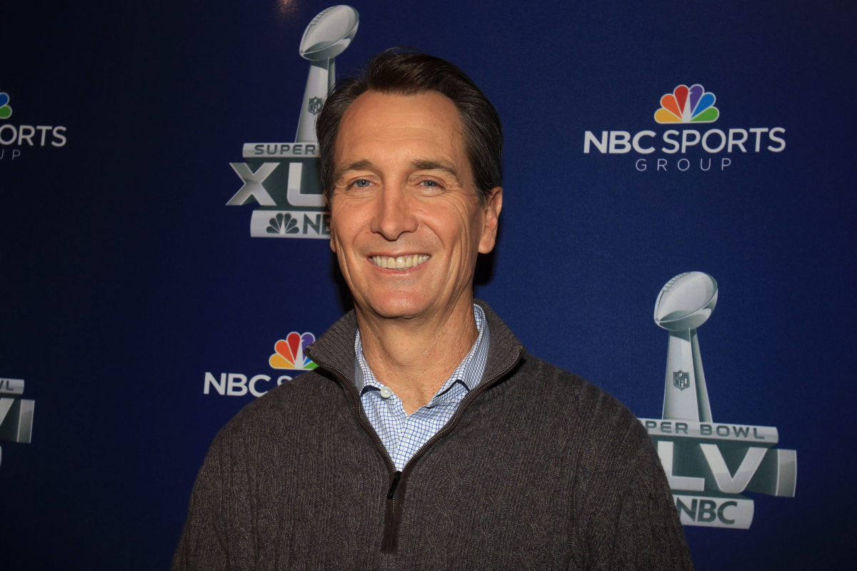 Cris Collinsworth smiling in front of a promo for the Super Bowl.
