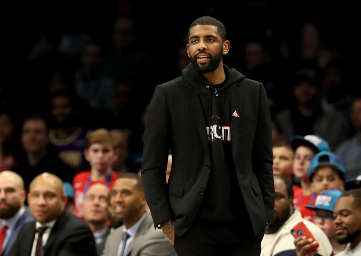 Kyrie Irving wearing all black standing on the sideline during a game.