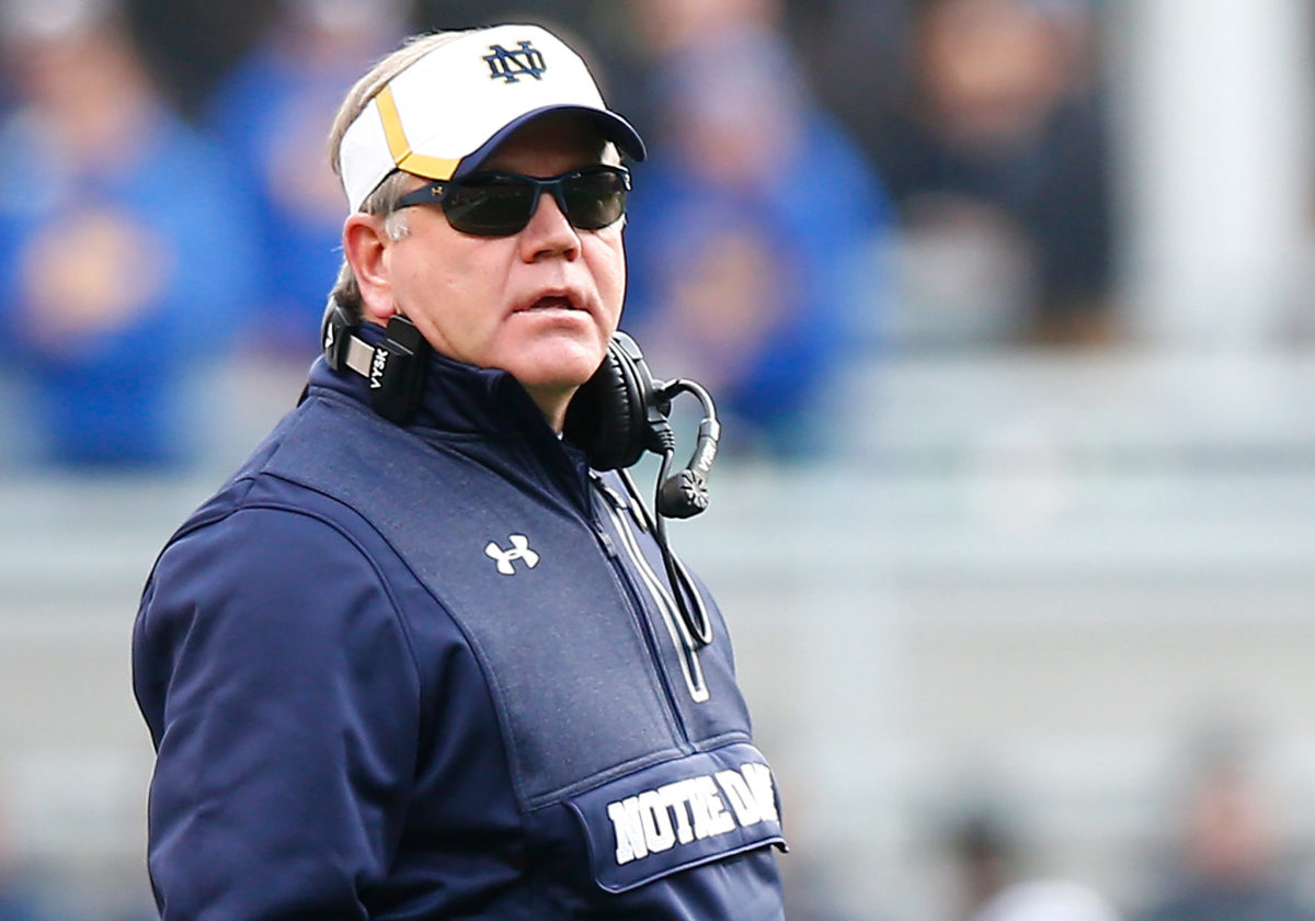 A closeup of Notre Dame coach Brian Kelly wearing sunglasses and a Notre Dame visor.