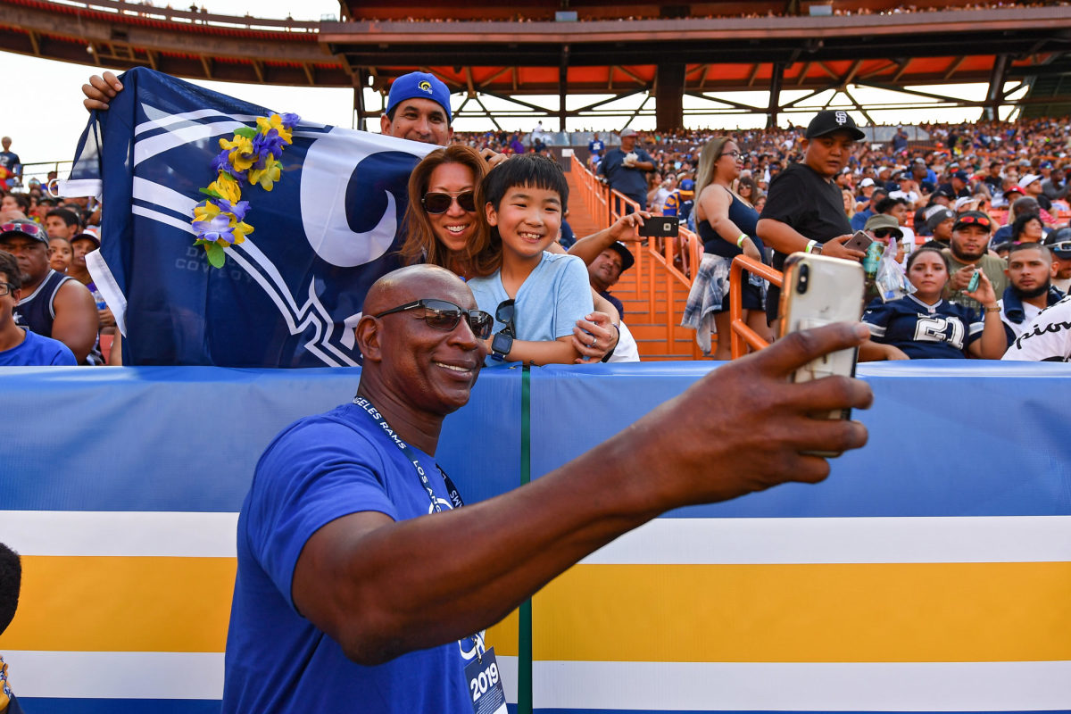 Eric Dickerson smiles and takes a selfie with Rams fans at a game.
