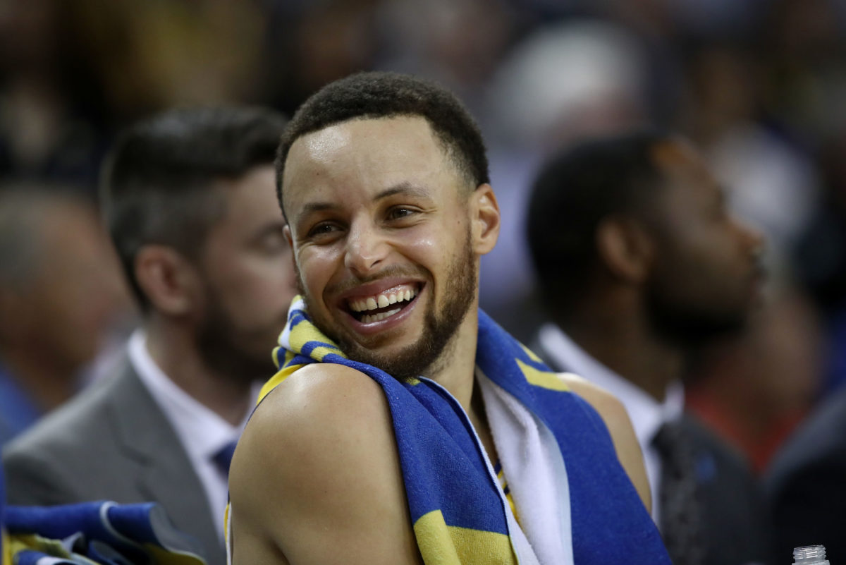 Stephen Curry laughing while sitting on the bench.