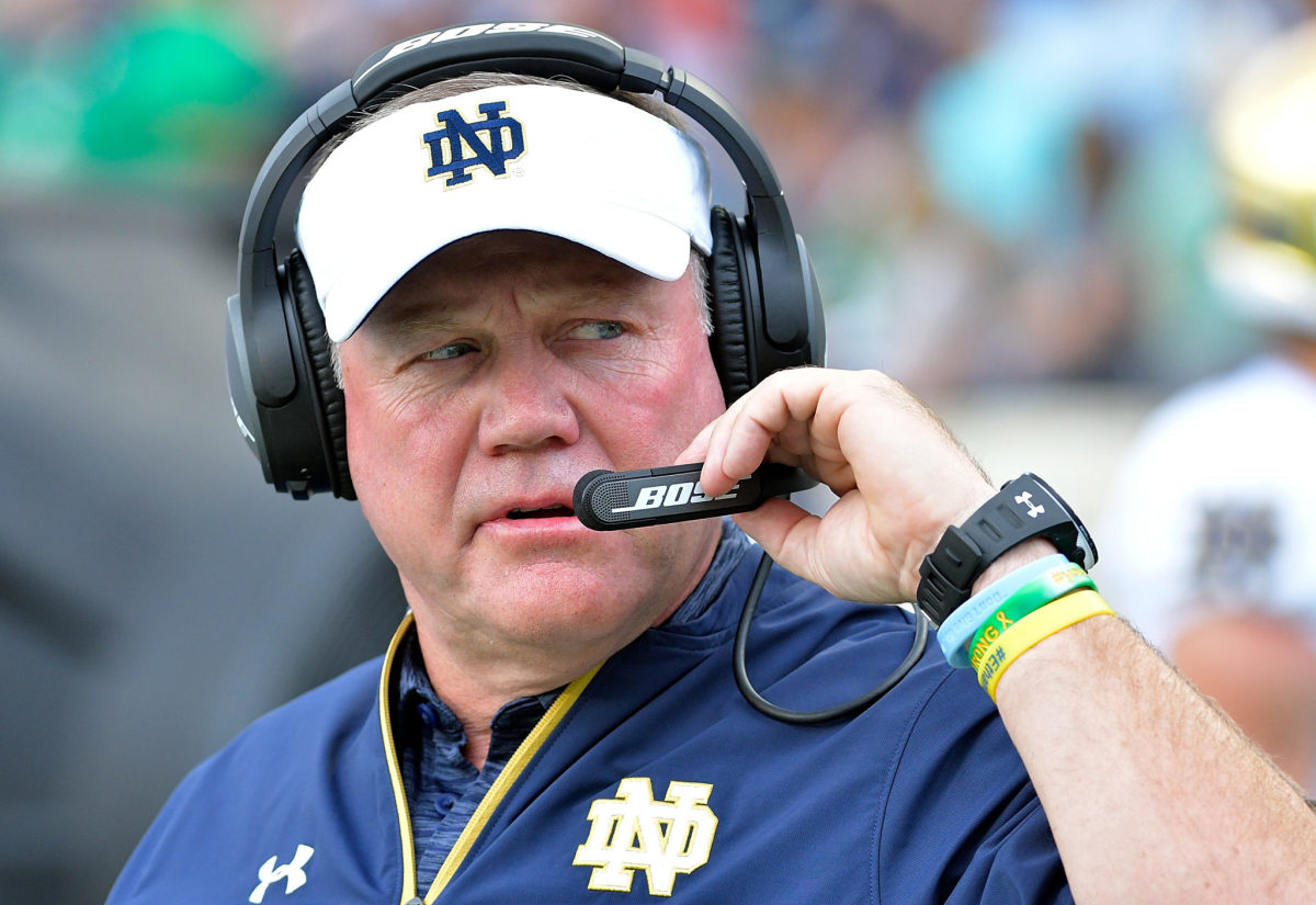 An extreme closeup of Brian Kelly wearing a Notre Dame hat and a head set.