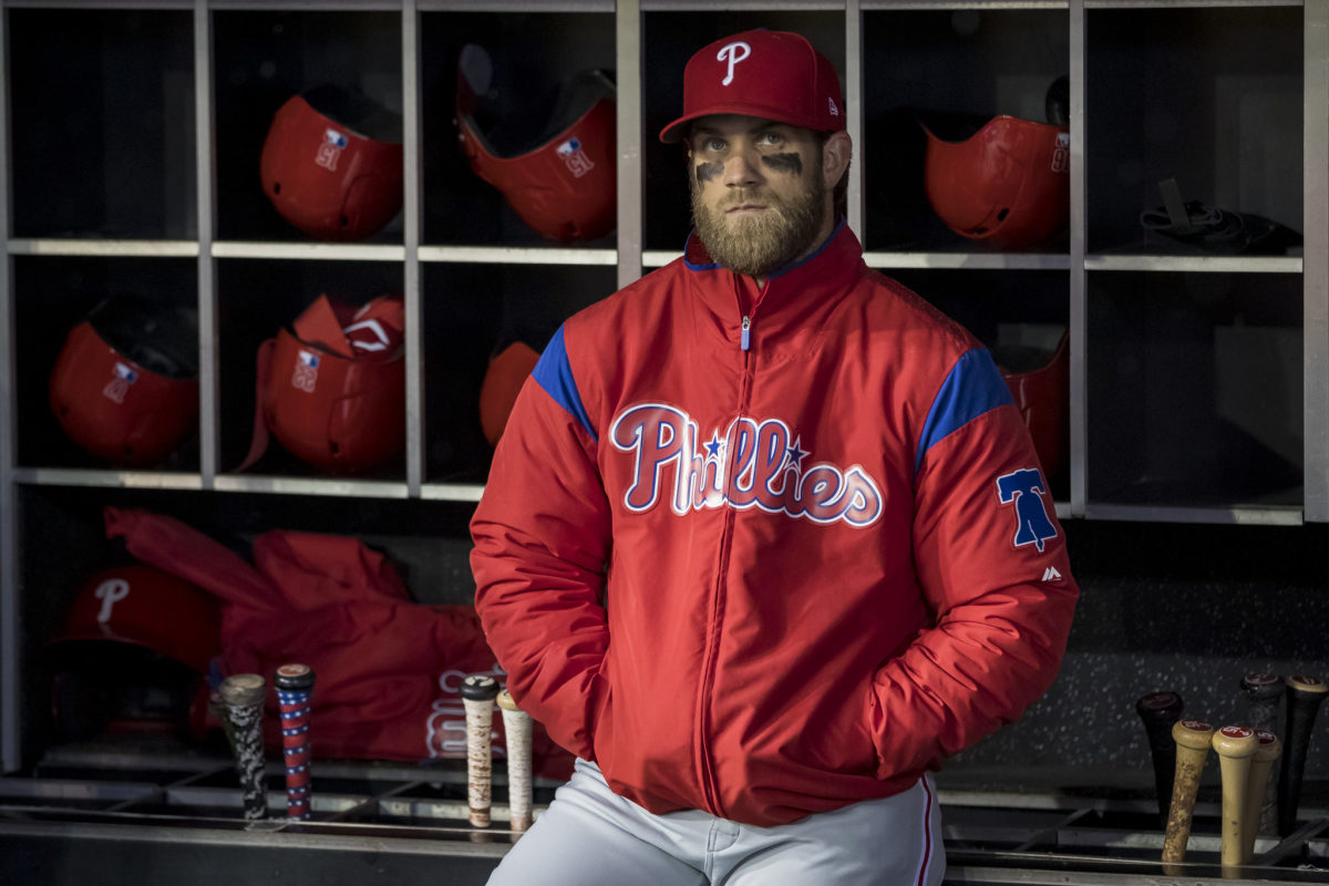 Bryce Harper standing in the dugout wearing his Phillies jacket.