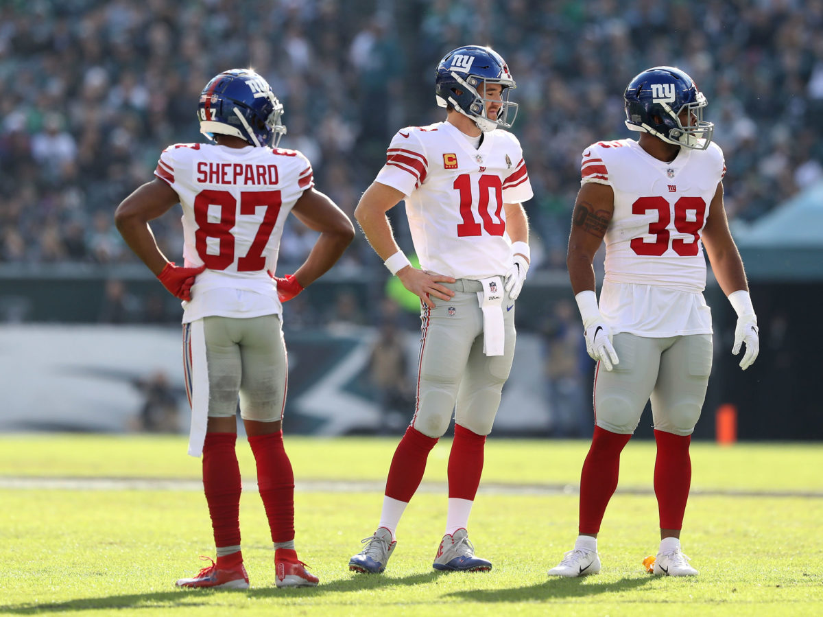 Eli Manning standing on the field with Sterling Shepard and Elijhaa Penny.