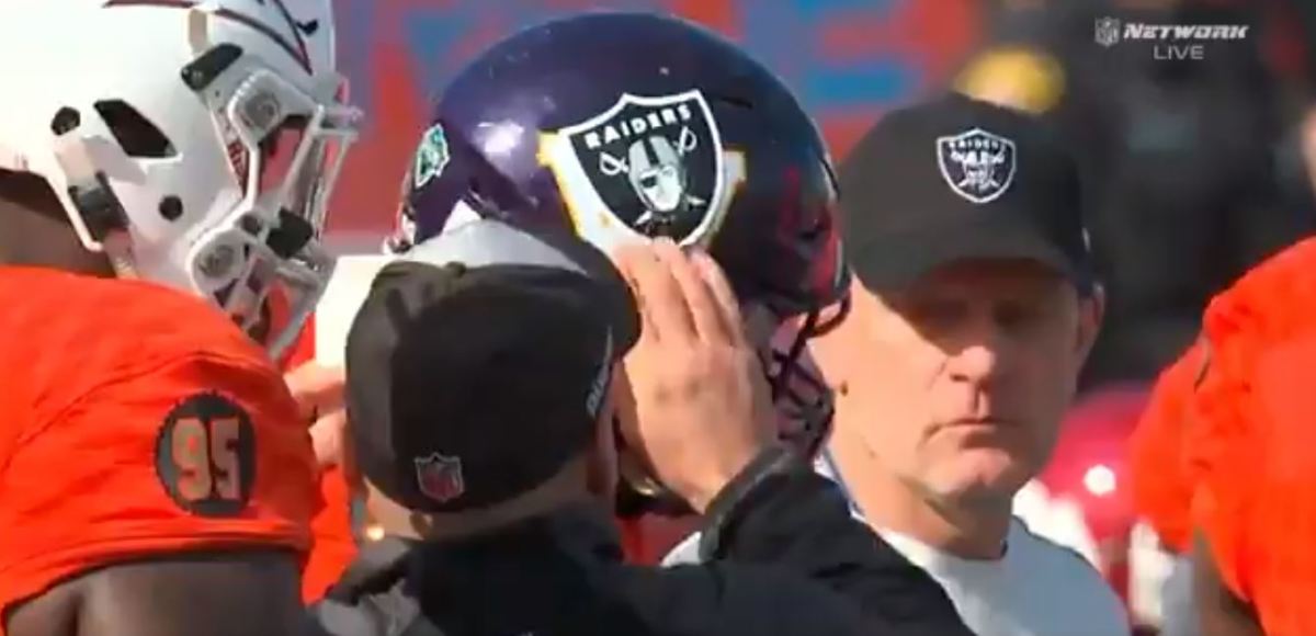 Jon Gruden puts a Raiders logo on a player's helmet at the Senior Bowl.