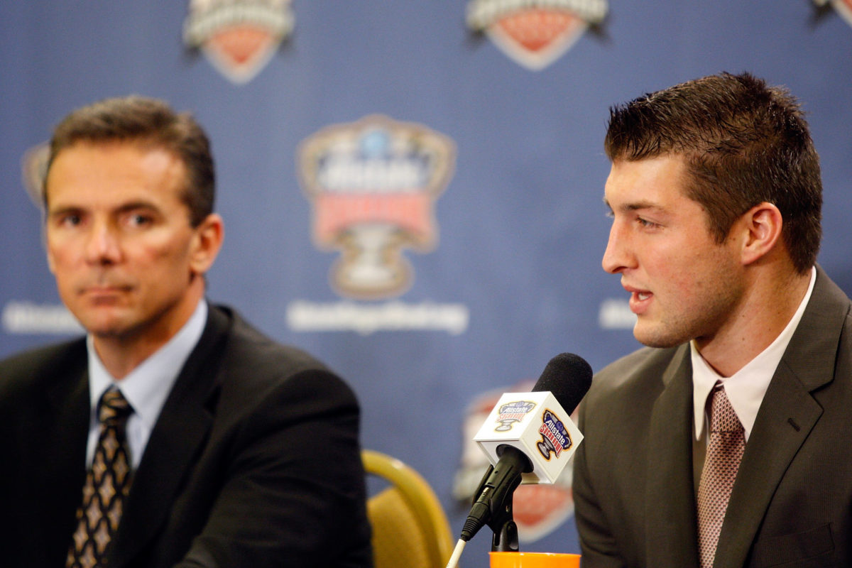 Tim Tebow speaking at a press conference with Urban Meyer by his side.