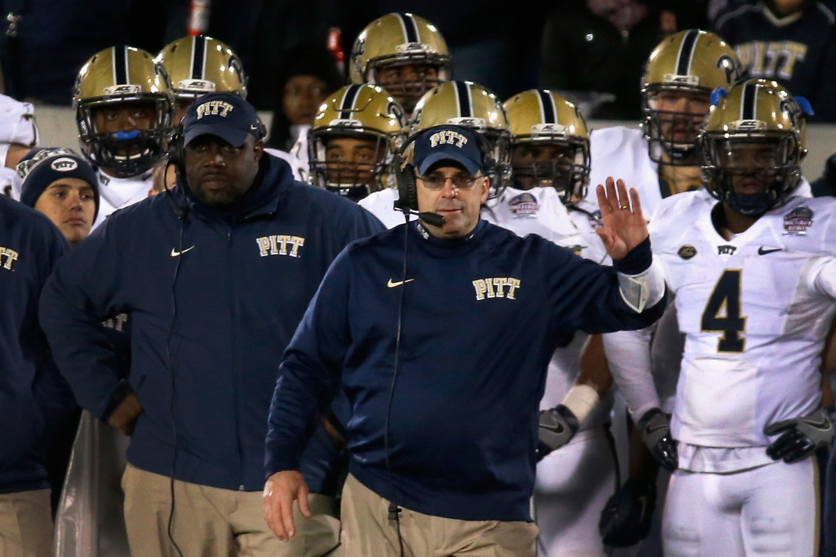 Pat Narduzzi holding his left hand up while his players stand behind him.
