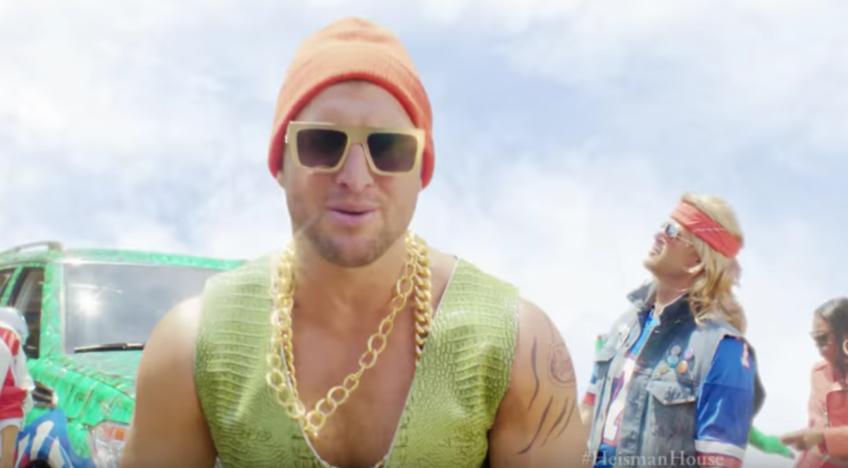 Tim Tebow wearing an orange beanie, a gold chain and a green vest in a commercial.