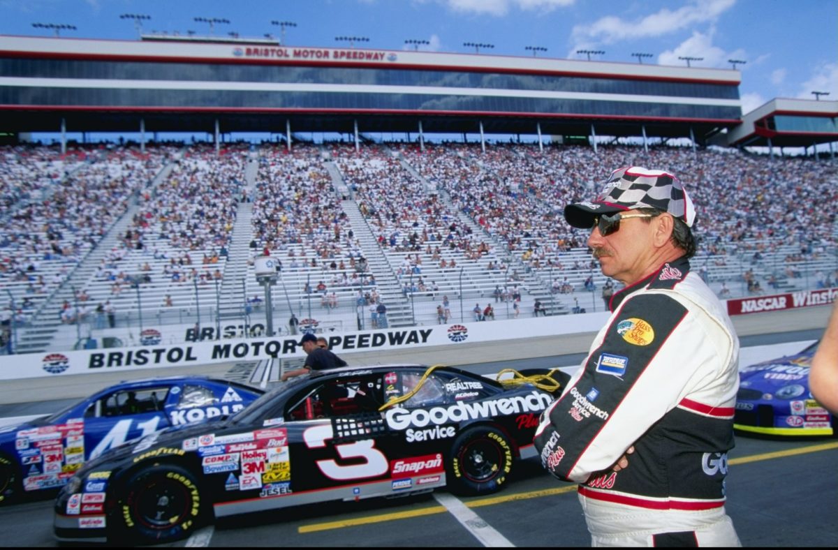 Dale Earnhardt Sr. stares to his left while standing in front of his race car.