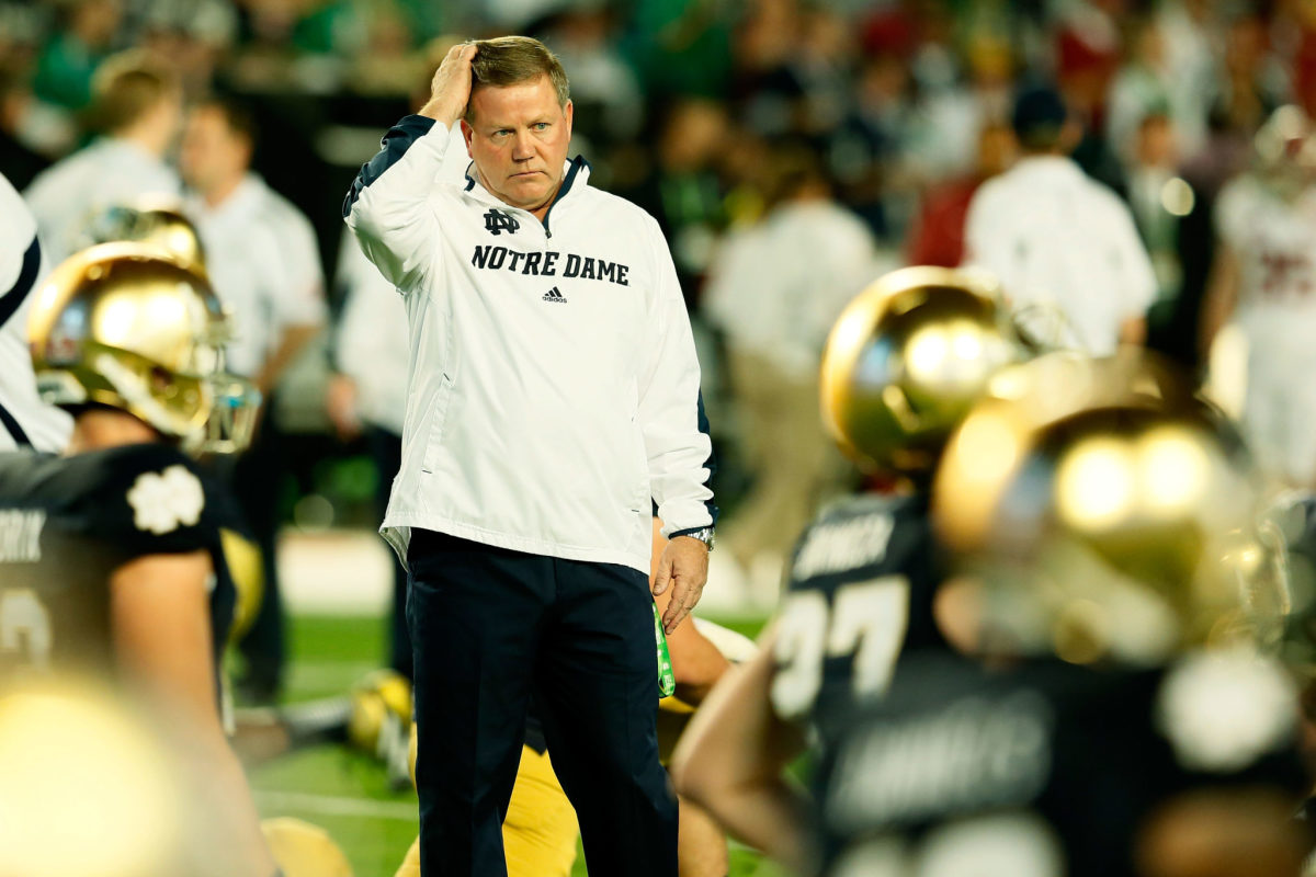 Brian Kelly standing with his Notre Dame players as they stretch before a game.