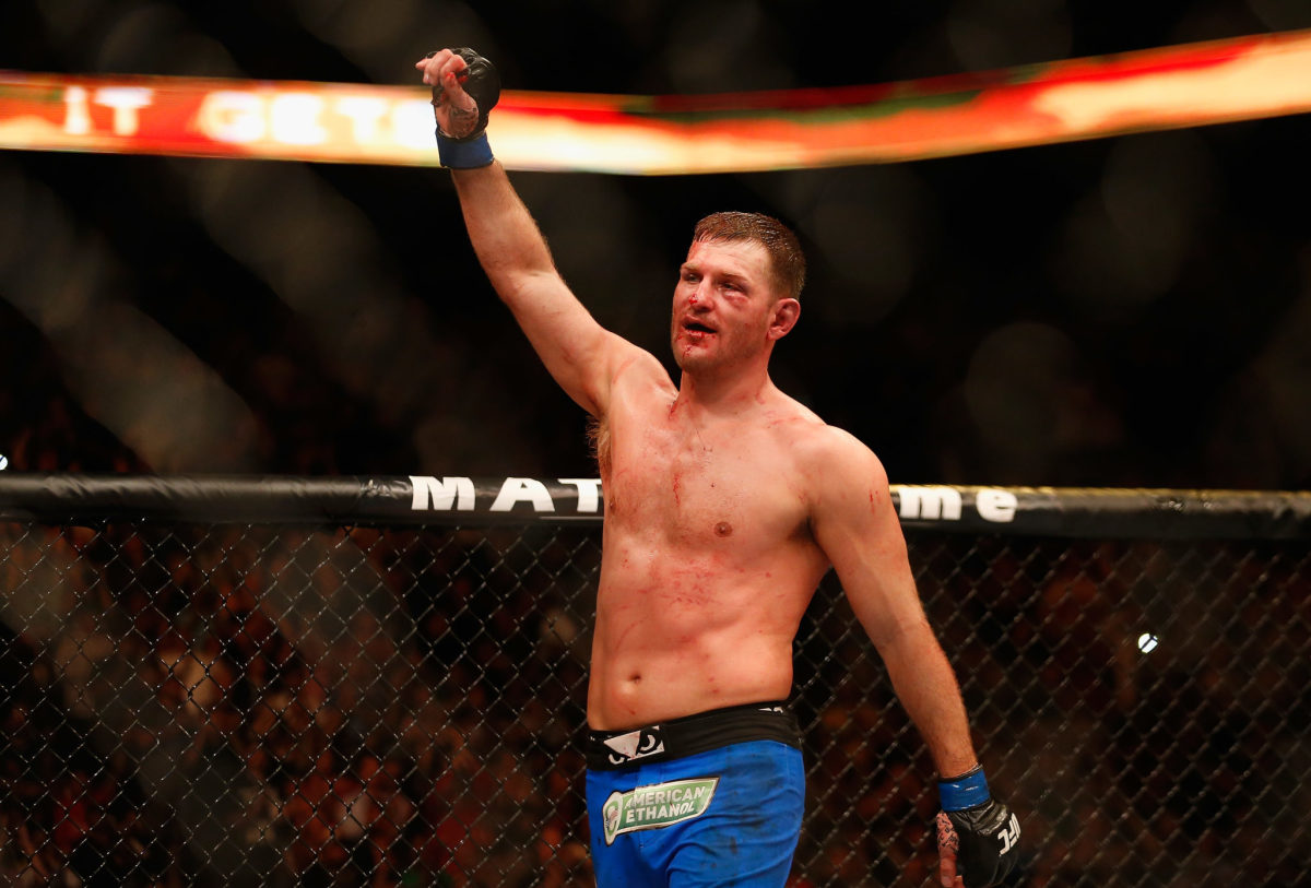 A bloodied Stipe Miocic raising his arms after a fight.