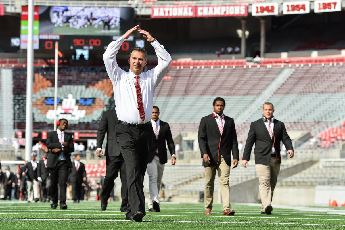 Urban Meyer making an O shape with his arms as he walks onto the football field.