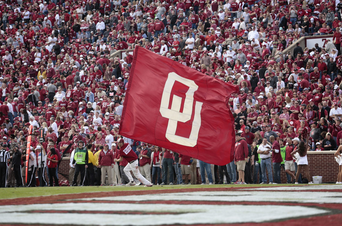 An Oklahoma cheerleader running with an OU flag in his hand.