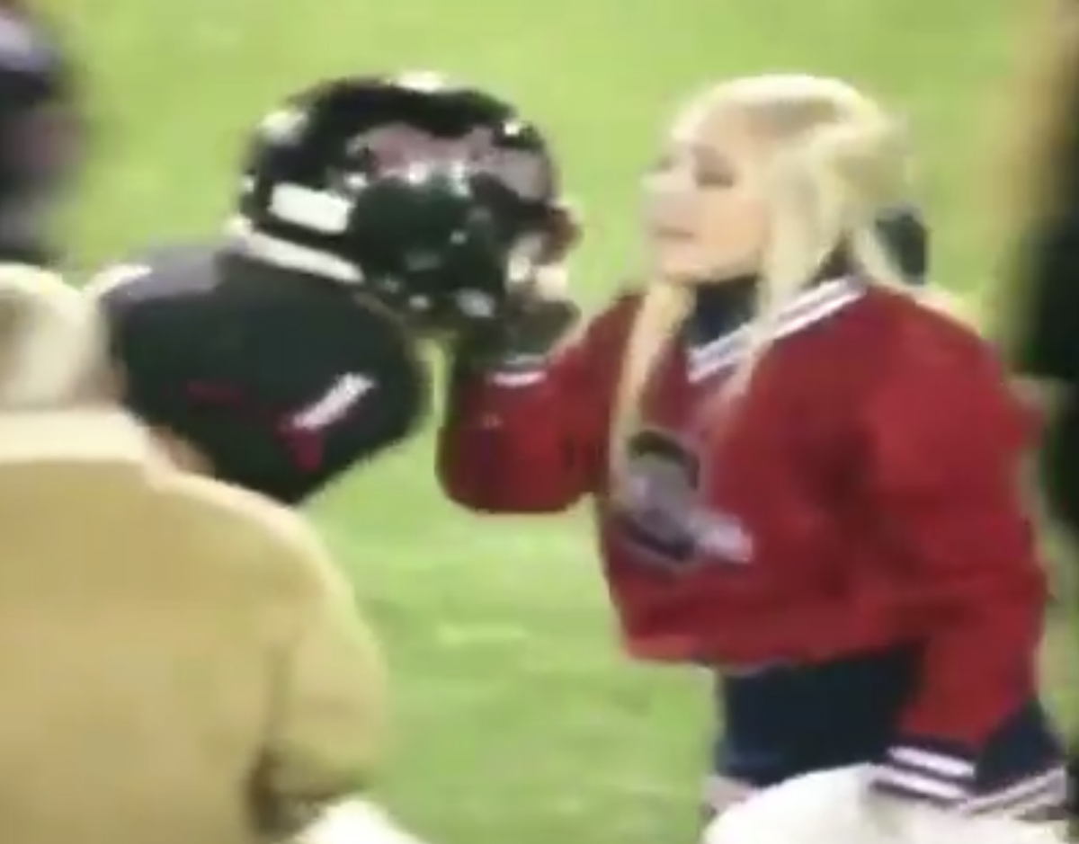 High school cheerleader pulls her football-playing boyfriend's facemask.
