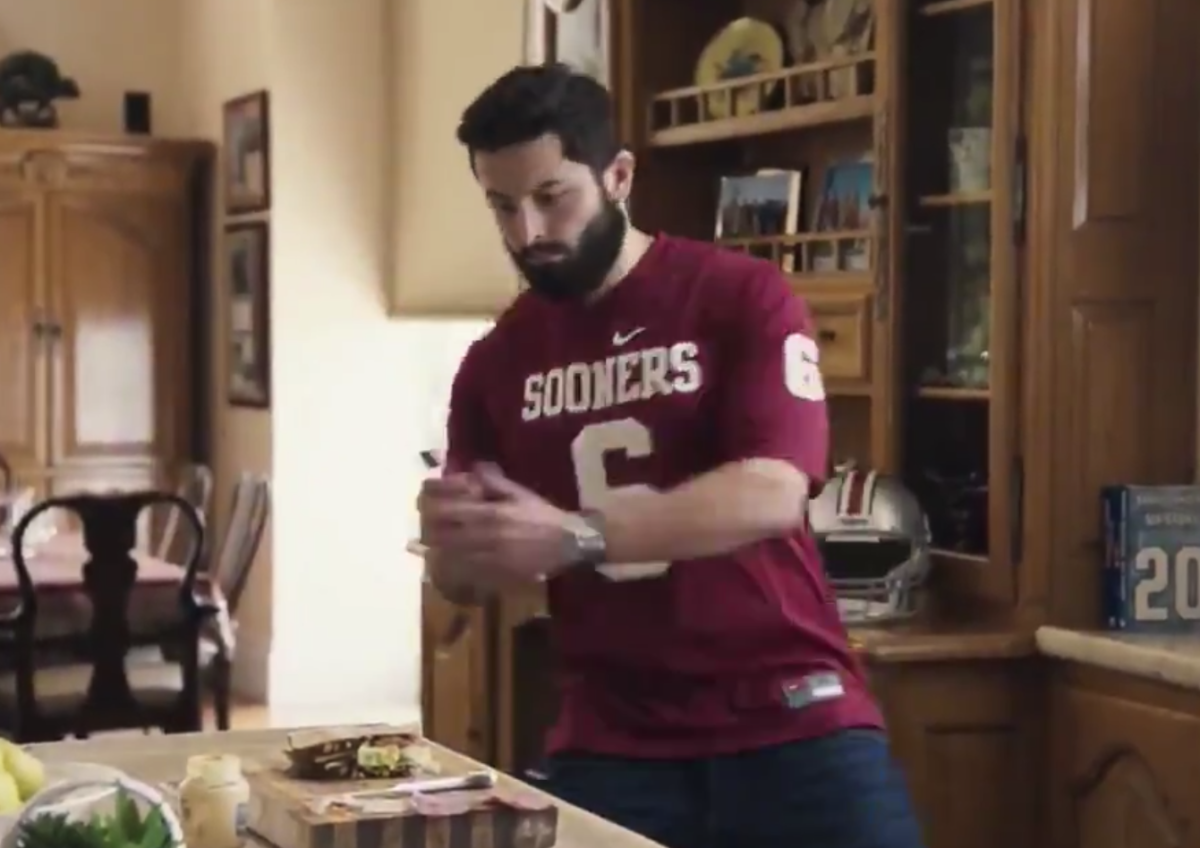 Baker Mayfield plants a flag in a sandwich for the Heisman House.