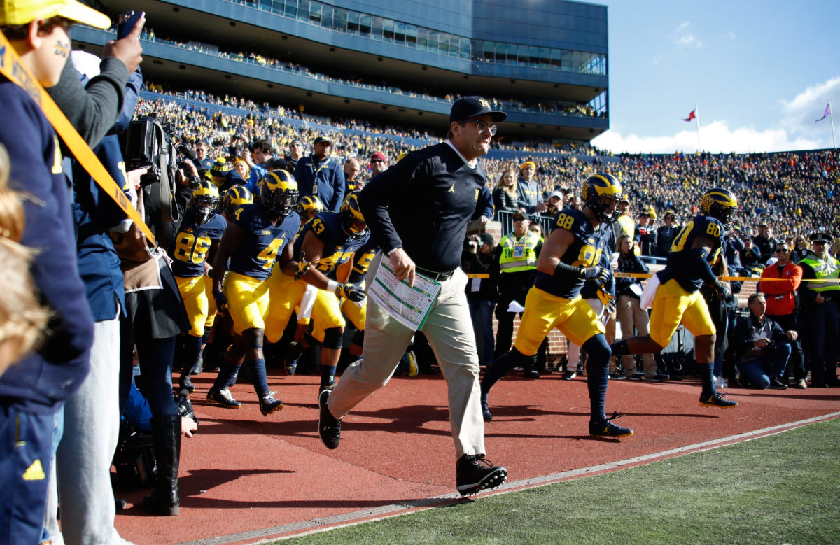 Head coach Jim Harbaugh of the Michigan Wolverines leads the team onto the field to play the Illinois Fighting Illini.