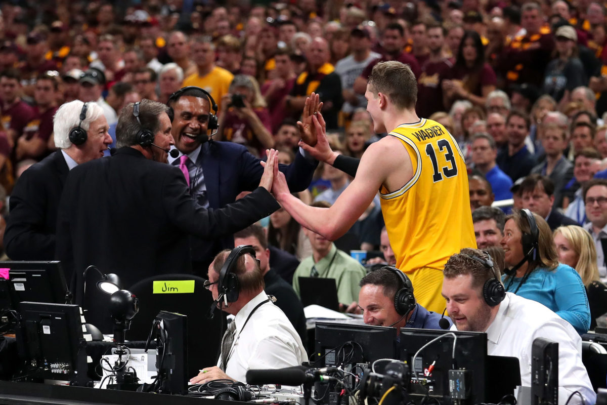Moe Wagner of the Michigan Wolverines high fives TV personalities Jim Nantz, Bill Raftery and Grant Hill after jumping off the court in the second half against the Loyola Ramblers during the 2018 NCAA Men's Final Four Semifinal.