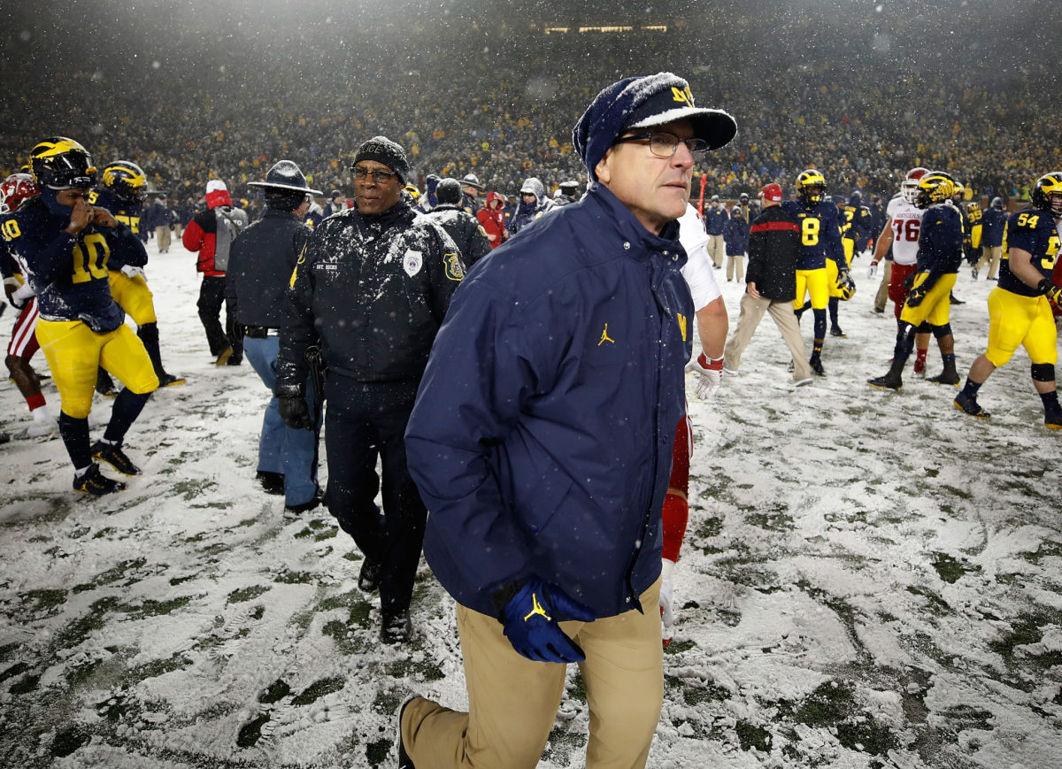 Jim Harbaugh walking off the football field after a Michigan game in the snow.