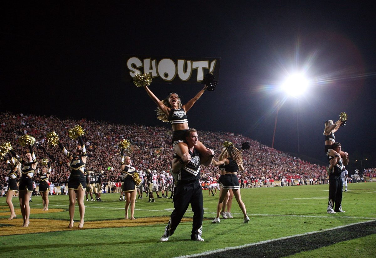 A Purdue cheerleader holding up a sign that says "Shout!"