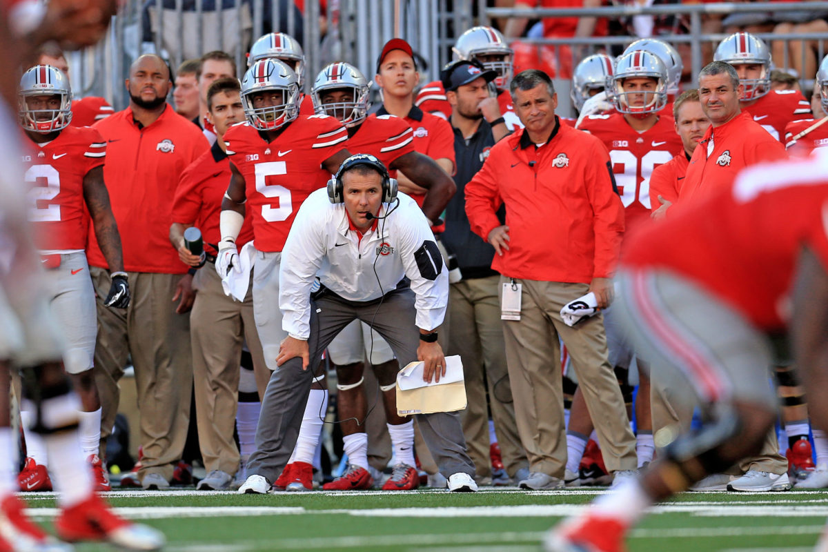 Urban Meyer crouching on the sideline during a football game.