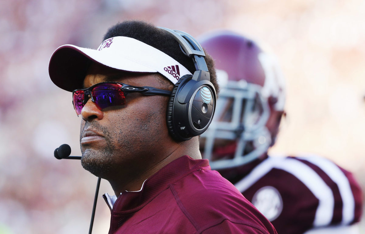 A closeup of Kevin Sumlin wearing a Texas A&M visor and sunglasses.