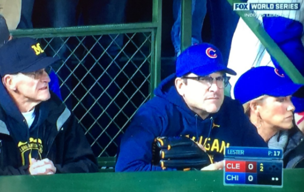 Jim Harbaugh in attendance at the Cubs game wearing a hat and glove.