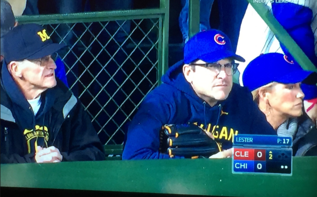 Jim Harbaugh in attendance at the Cubs game wearing a hat and glove.