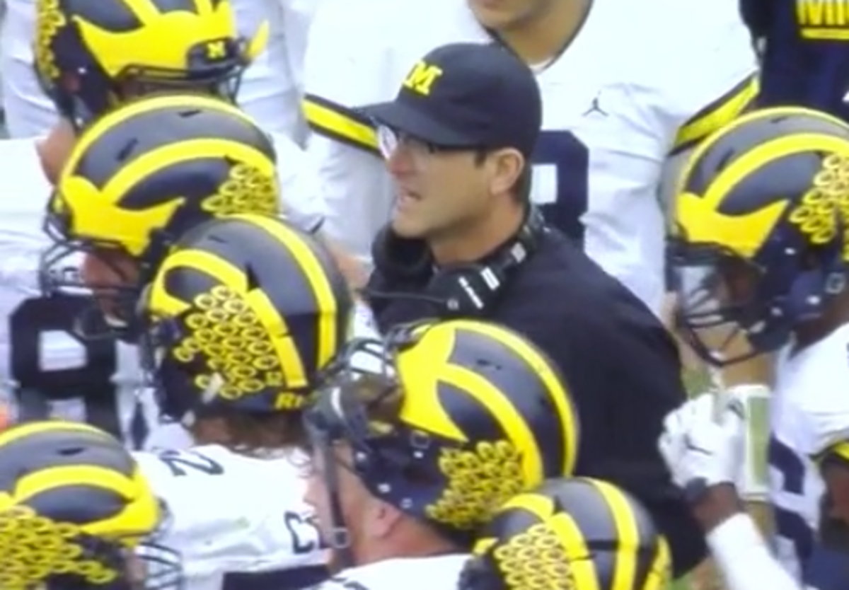 Jim Harbaugh standing with Michigan players on the sideline.