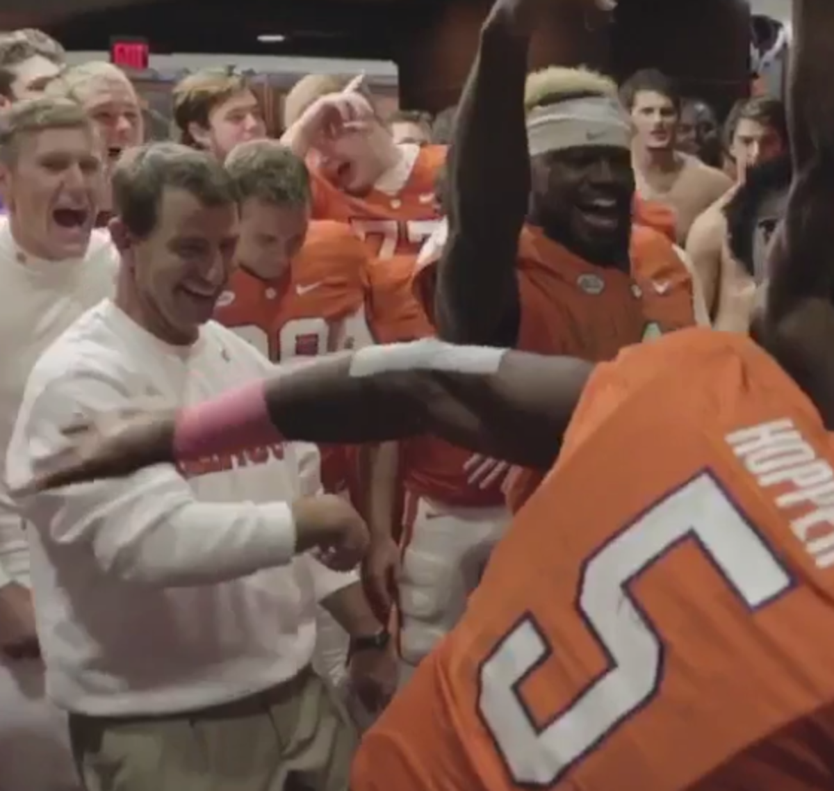 Dabo Sweeney laughing in the locker room as players dance.