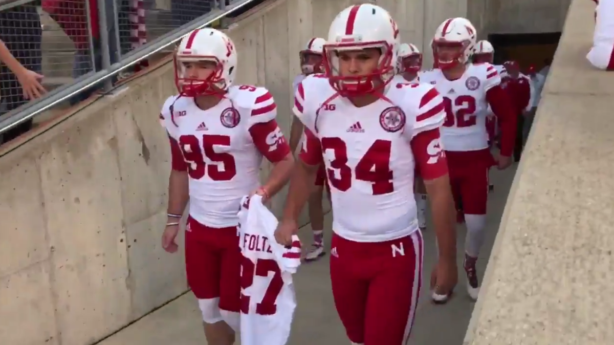 Nebraska players walking on the field holding Sam Foltz uniform.