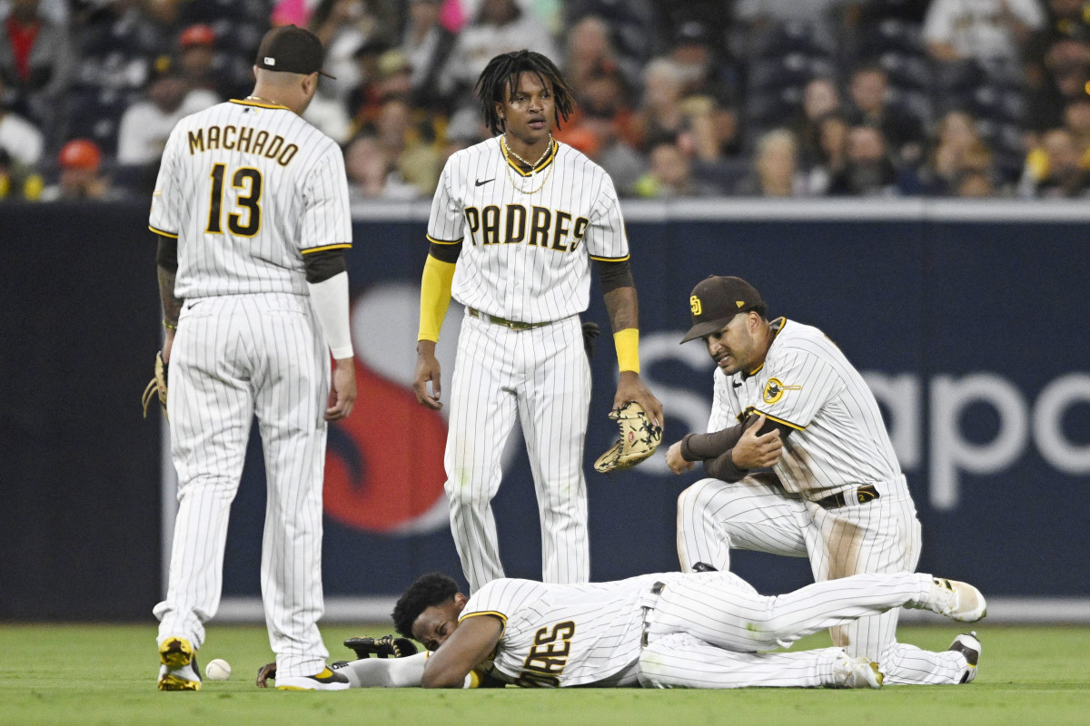 SAN DIEGO, CA - JULY 7:   Jurickson Profar #10 of the San Diego Padres (C) lies on the ground as Manny Machado #13 (L), C.J. Abrams #77 and Trent Grisham #2 look on during the fifth inning of a baseball game against the San Francisco Giants July 7, 2022 at Petco Park in San Diego, California. Profar was injured on the play. (Photo by Denis Poroy/Getty Images)