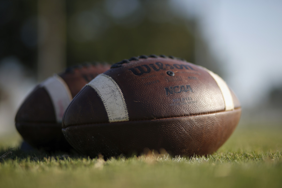 A closeup of two footballs on the grass.